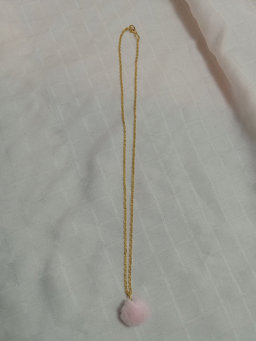 Handmade necklace with a small pom-pom and gold-colored accent hooks and chains